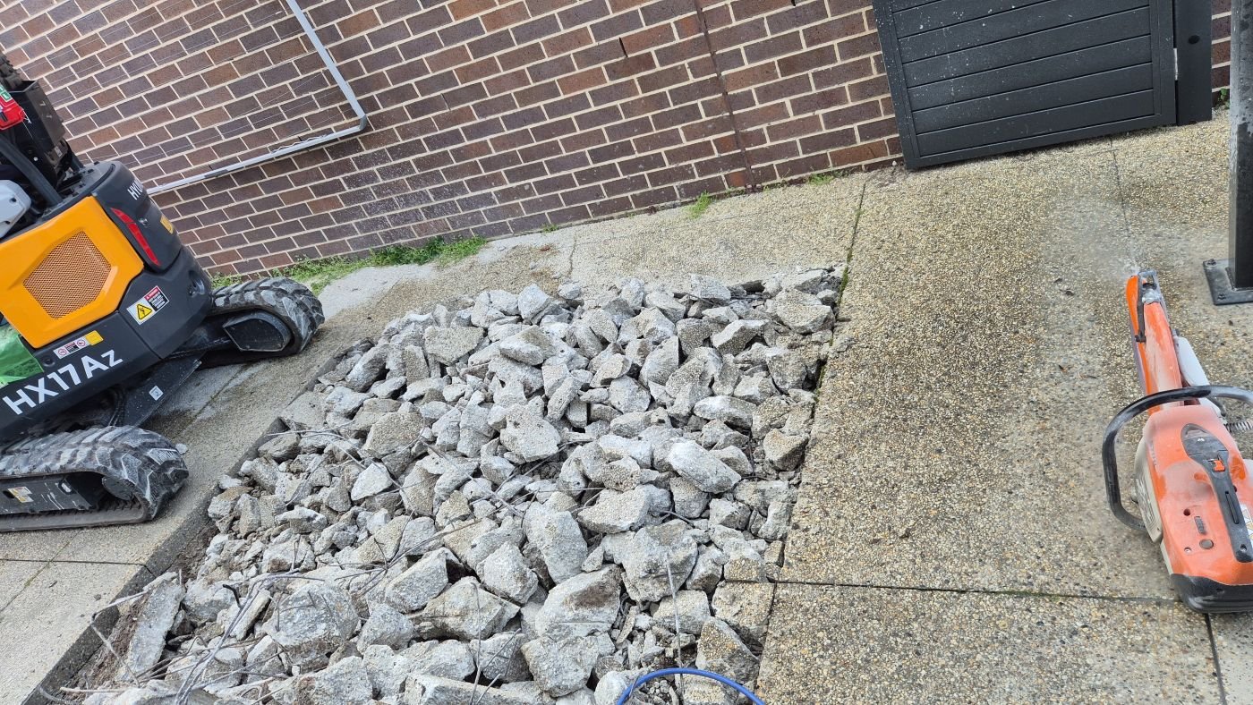 Mini excavator beside old concrete broken out and ready for removal